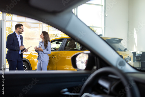 Super sales team in dealership, two consultants or managers in elegant suits with laptop and tablet in arms in car dealership