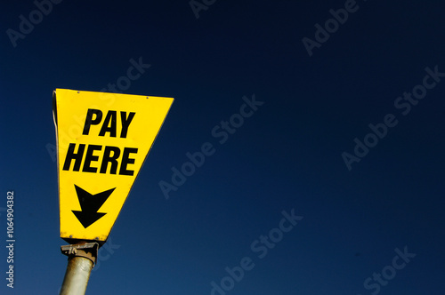 Pay Here sign in car park against blue sky.