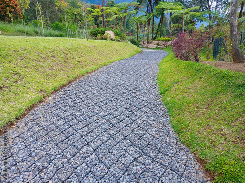 The view of a gravel pathway in a garden park located in a mountainous area, surrounded by lush greenery and vibrant plants, creating a serene and picturesque setting