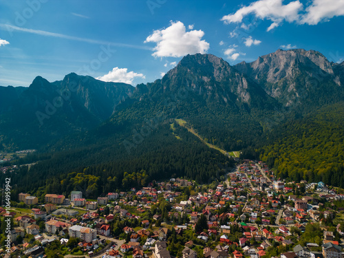 A town at the base of the mountain in the autumn season. Astonishing aerial view with the rocky mountains filmed in cinematic style. Romanian landscape above Busteni city in a sunny day with blue sky photo