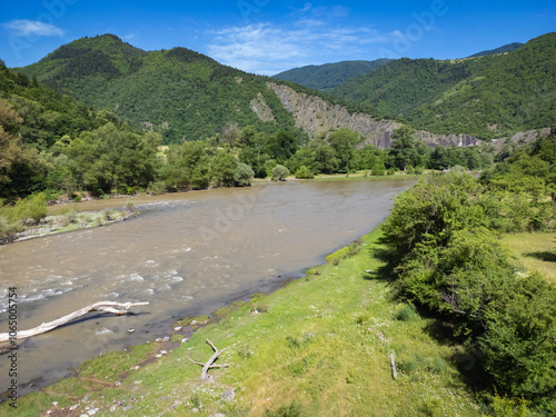 Drone view of a mountain river with brown water against the background of mountains on a sunny day