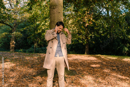 Mediterranean handsome man in a trench coat talking on the phone in autumn park, on-call outside photo