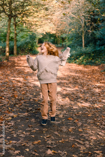 red-haired excited happy smiling child girl in a warm cozy sweater jumping in the air with excitement and joy in an autumn park photo