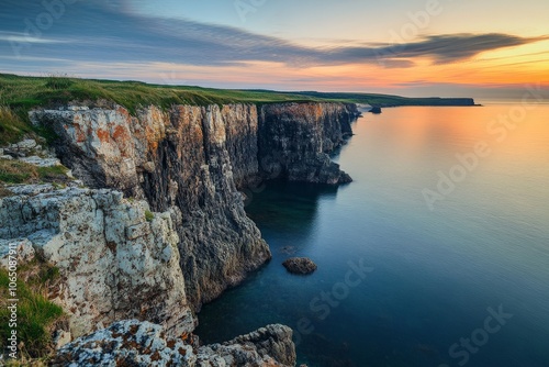 A stunning rugged cliff edge at sunset overlooks a calm ocean, capturing nature's beauty and tranquility in a breathtaking coastal landscape scene. photo