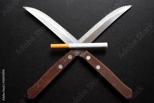 a tobacco filter cigarette lying on 2 knifes with wooden handles, on black table. selective focus