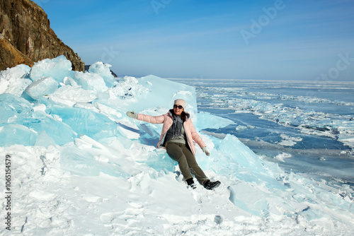 A happy traveler is sitting on a huge block of ice. Hummocks on the ice of frozen Lake Baikal on a sunny winter day. photo