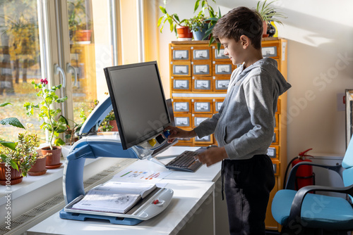 A young boy in an inclusive library reads with the help of an electronic magnifier. This image emphasizes themes of blindness, inclusivity, disability, and accessible education for visually impaired 