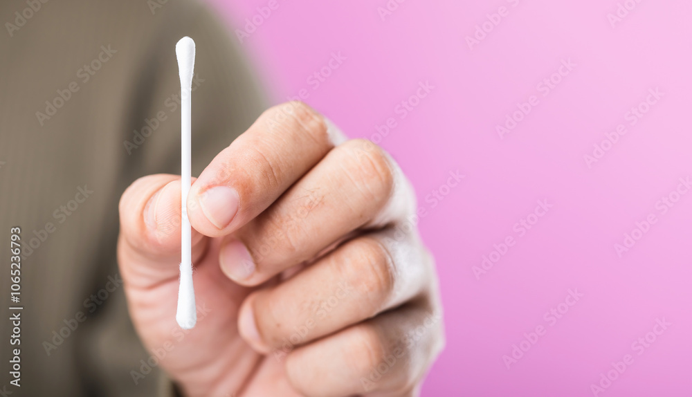 A close-up of a person holding a cotton swab against a pink background ...