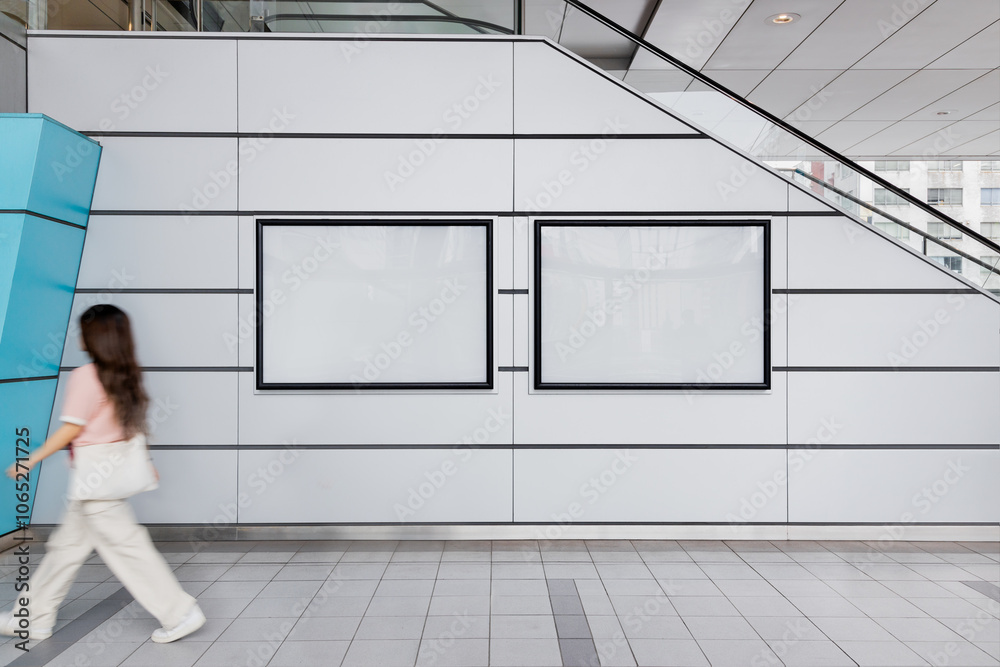 A young woman walks in front of two blank billboard posters displayed down an escalator in a metro station. Ideal for advertising and mockup