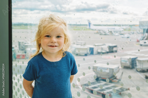 Cute little toddler girl at the airport, traveling. Happy healthy child waiting near window and watching airplanes. Family going on summer vacations by plane.