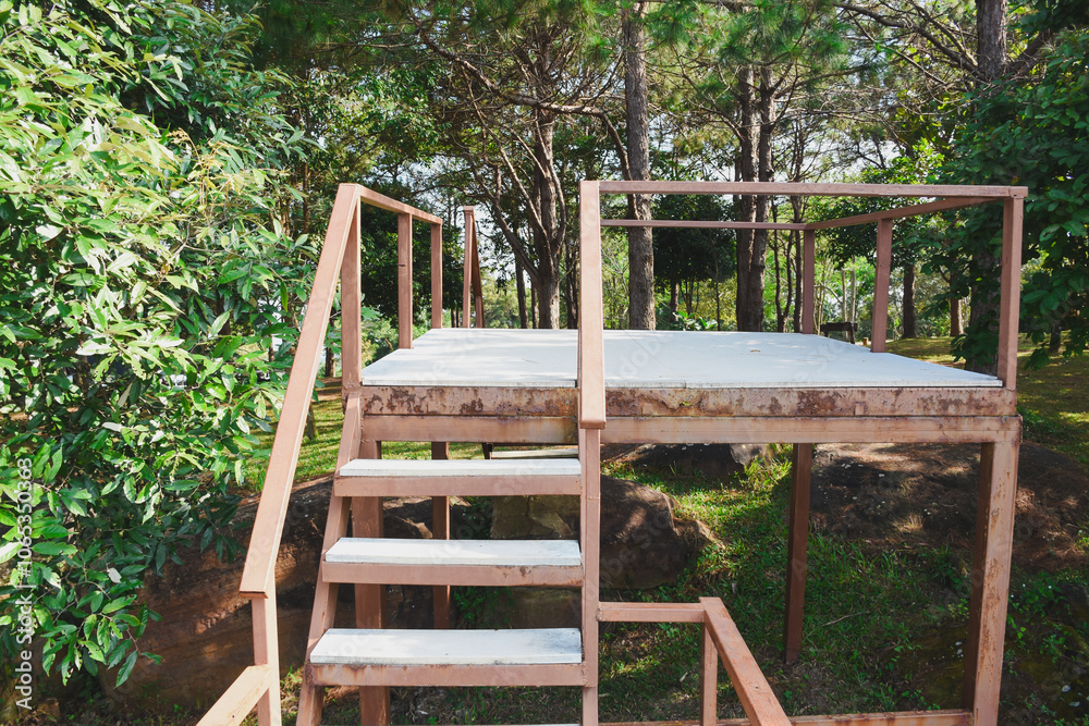 wooden platform with a set of stairs leading up to it. The platform is elevated and has a simple railing around it. The structure is situated outdoors, surrounded by trees and greenery wooden platform with a set of stairs leading up to it. The platform is elevated and has a simple railing around it. The structure is situated outdoors, surrounded by trees and greenery