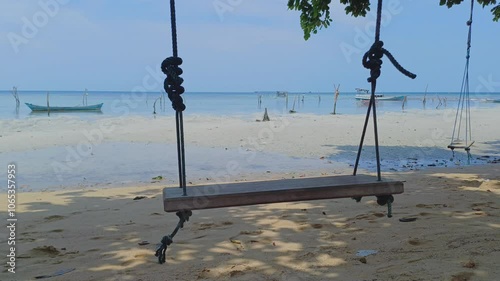 empty wooden swing swinging on the beach with calm wavy white sand, blue sky, receding beach