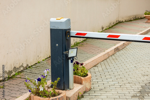 Automated barrier gate at an entrance with flowers, located in a well-maintained driveway.