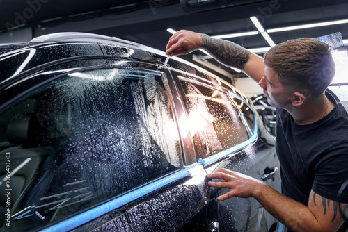 A tattooed man applies protective film to a black car