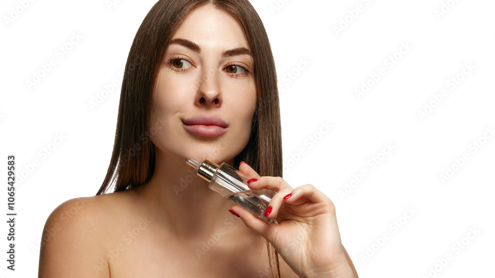 Fototapeta premium Pretty woman with bare shoulders holding serum bottle to her face for skincare against white background. Facial care treatment. Concept of beauty, healthcare, freshness and wellness, confidence. Ad