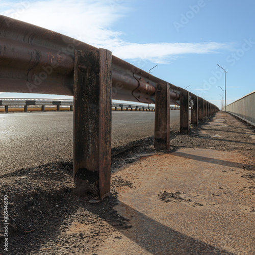 Low-angle view of metal guardrail on bridge with asphalt walkway and blue sky background. Urban safety infrastructure concept.