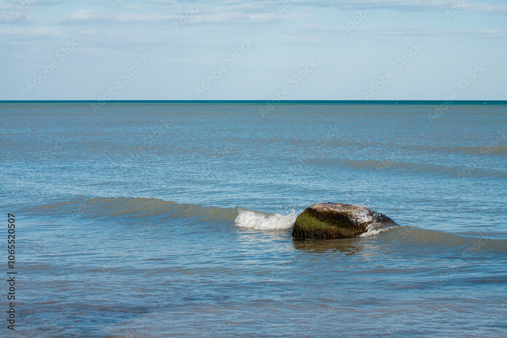 Fototapeta premium The singular boulder in Lake MIchigan breaks the incoming waves just offshore of Harrington Beach State Park, Belgium, Wisconsin