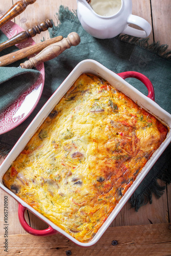 Oven baked omelette with vegetables served with sour cream on wooden background.