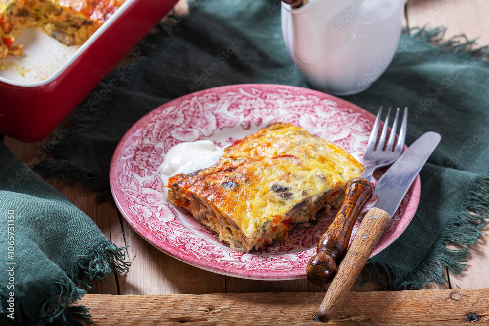 Oven baked omelette with vegetables served with sour cream on wooden background.