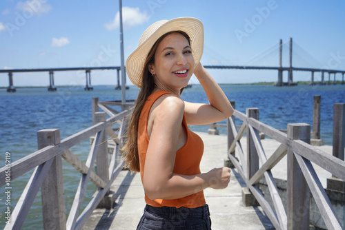 Visiting Northeast Brazil. Young woman turns around on pier in Aracaju with Ponte Joao Alves bridge on the background, Brazil. photo