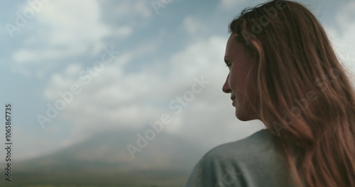 A woman with long hair stands in a strong pose against a backdrop of dark clouds in the sky. Her hair blows in the wind as she gazes into the distance. photo