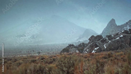 Panning shot across mountains obscured by a snowstorm and pull focus to desert sagebrush in Castle Rocks State Park, Idaho