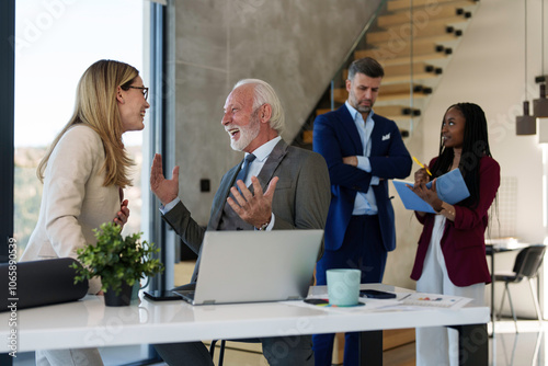 Focused Caucasian businessman types on a laptop in a modern office setting, his professional attire indicating a corporate environment, with colleagues engaging in the background.