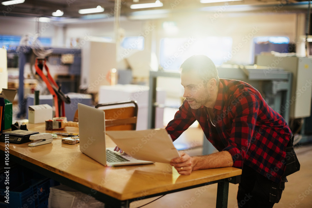 Young man using a laptop while working in a printing press office Young man using a laptop while working in a printing press office