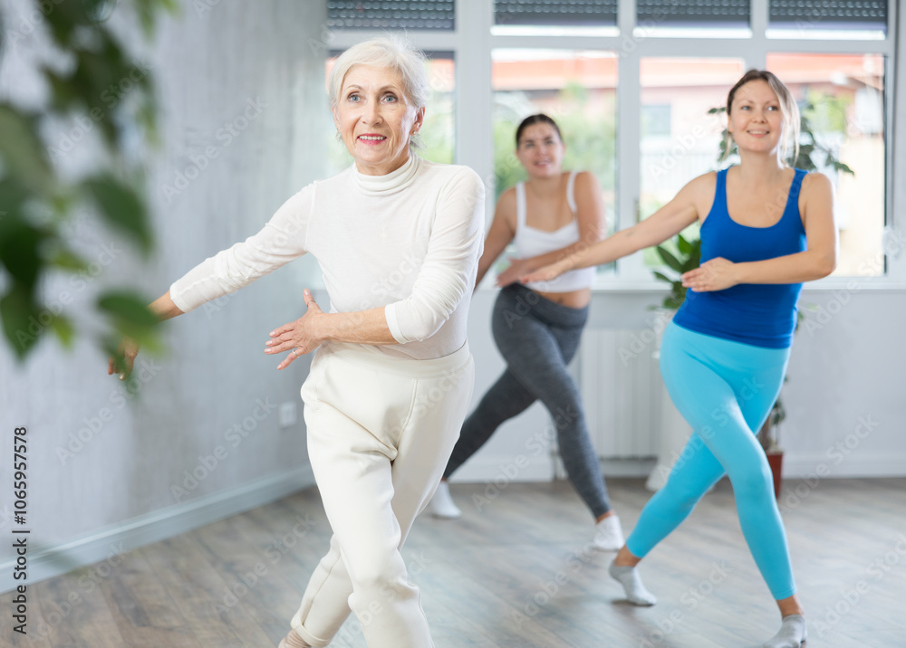 Obraz premium Energetic women of different ages warming up with dancing elements before training together in fitness center