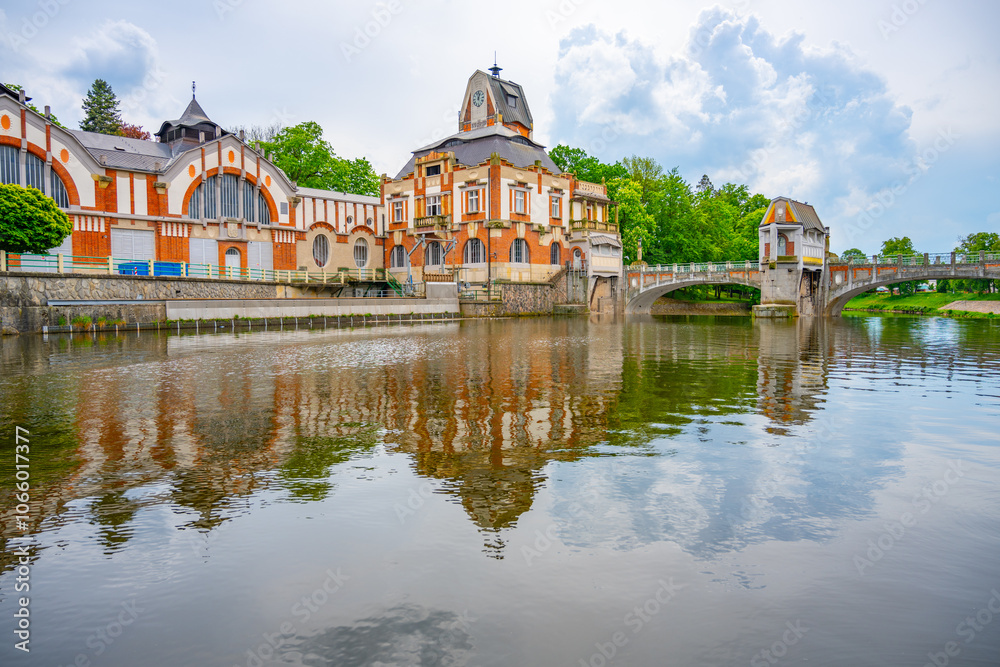 Fototapeta premium The picturesque Art Nouveau hydroelectric power station stands by the calm river in Hradec Kralove, Czechia, reflecting its unique architectural beauty against the serene water and surrounding