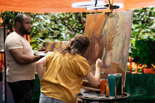 Team of artists painting a beautiful rustic creation on canvas, mixing colors together on a palette to create a nature inspired design. Diverse painters enjoy quality time in art studio. photo