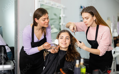 Two young women working in a beauty salon as a make-up artist and a hairdresser serve a young female client photo