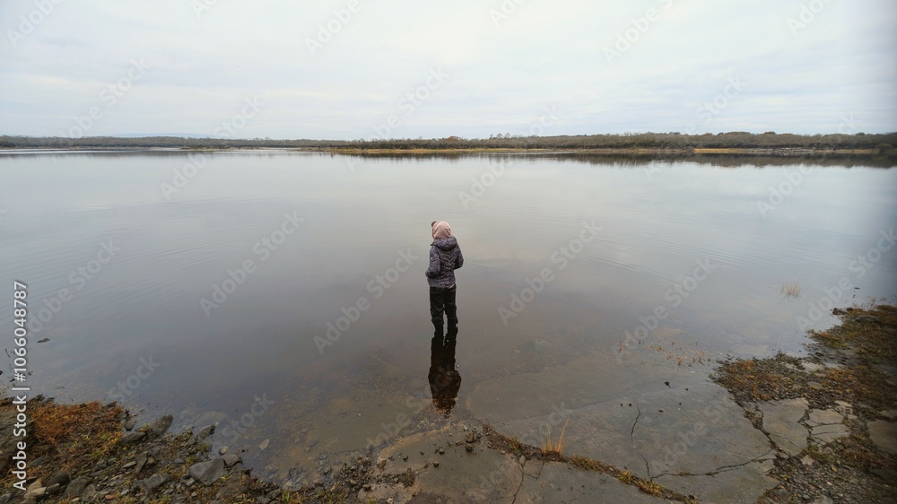 Hiker girl standing on the rock reflected in lake at Coole park nature reserve, County Galway, Ireland, nature background