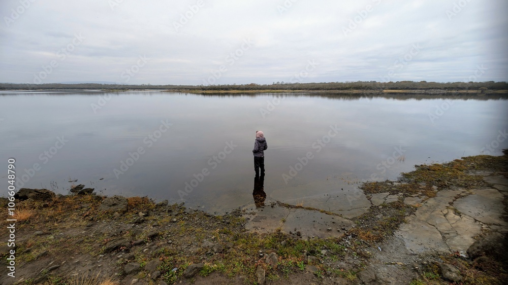 Hiker girl standing on the rock reflected in lake at Coole park nature reserve, County Galway, Ireland