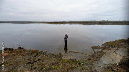 Hiker girl standing on the rock reflected in lake at Coole park nature reserve, County Galway, Ireland