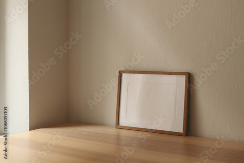 Horizontal wooden thin picture frame, empty poster mockup on wooden table near window. Beige wall background. Modern moody interior decor. Side view, copy space, no people. Minimal composition.