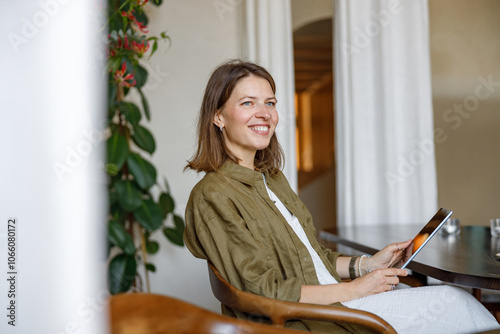 A cheerful woman relaxing with a tablet in a stylish caf surrounded by greenery