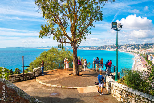 Fototapeta Naklejka Na Ścianę i Meble -  Tourists enjoy a summer day on Castle Hill overlooking the turquoise Mediterranean Sea, pebble beach, and the city of Nice France, on the Riviera Cote d'Azur.