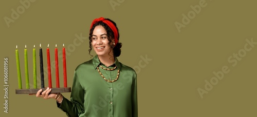 Young African-American woman with burning candles on green background with space for text. Kwanzaa celebration photo