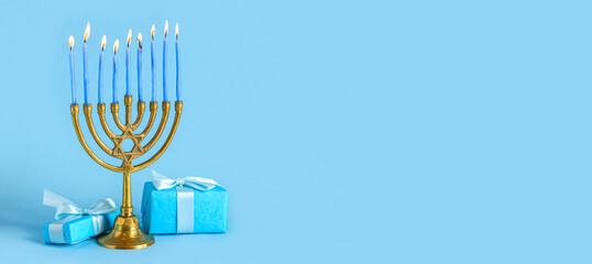 Menorah with burning candles and gifts for Hanukkah celebration on color background