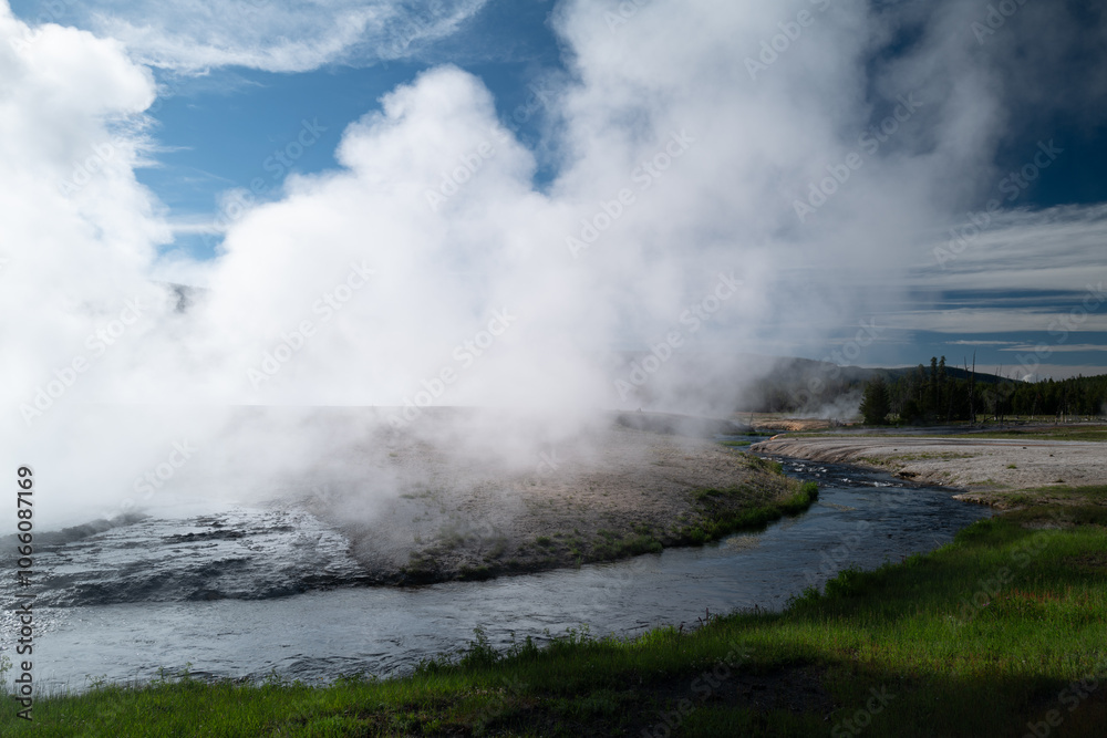 Obraz premium Steam pours from an opening in the Blacksand Basin of Yellowstone from a Geothermal spring and into a tributary of the Snake River