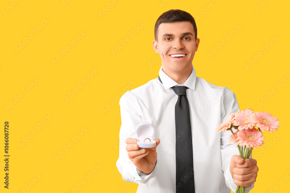 Handsome man with flowers and engagement ring on yellow background Handsome man with flowers and engagement ring on yellow background