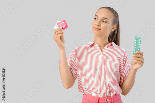 Thoughtful young woman with condoms and contraceptive pills on light background photo