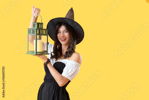 Young witch with lantern on yellow background photo