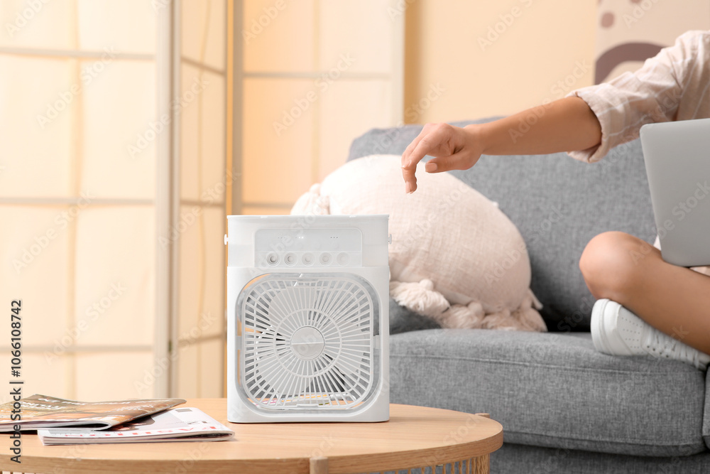 Φωτογραφία Beautiful young woman near portable table fan with humidifier in living room