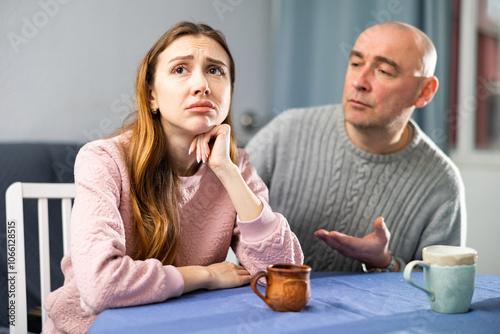 Caring european man tries to comfort his upset wife while sitting at a table in a room photo