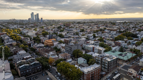 Wide aerial view capturing the neighborhoods of Hoboken and Jersey City, with the iconic New York City skyline stretching across the horizon in the background. Overcast skies add depth  photo