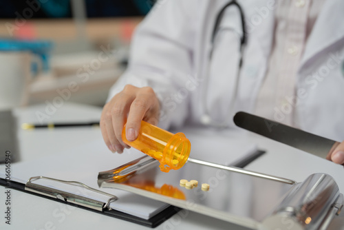 Doctor carefully pouring pills from orange bottle onto metal tray in pharmacy setting, highlighting importance of accuracy in medication preparation photo