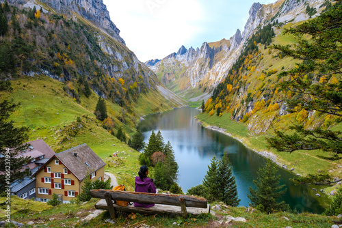 Nestled amidst stunning Swiss mountains, a person sits peacefully by Falensee, surrounded by vibrant autumn foliage. The tranquil water mirrors the breathtaking landscape, inviting contemplation. photo