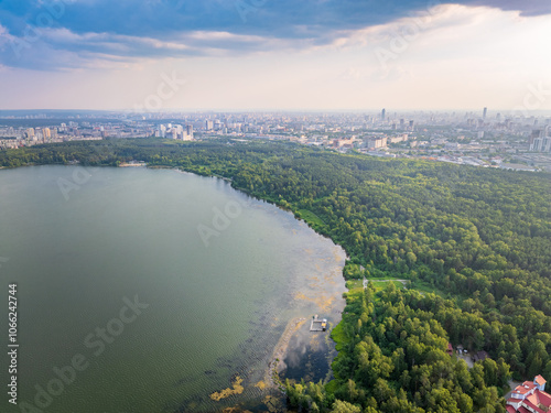 Big lake with green shores in bright sun light and city on horizon, aerial landscape. Recreation concept. Aerial view photo